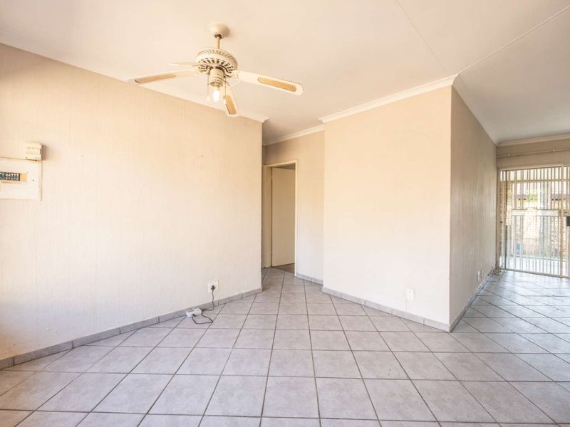 An empty, tiled living area featuring a ceiling fan, neutral walls, and a security gate leading to the exterior.