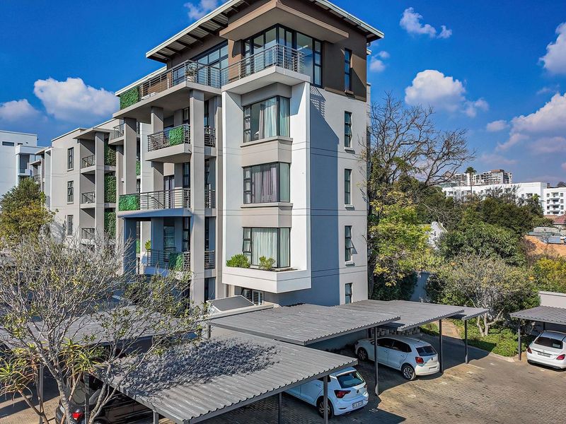A modern multi-story apartment building featuring private balconies, vertical landscaping, and dedicated covered parking bays within a well-maintained residential complex.
