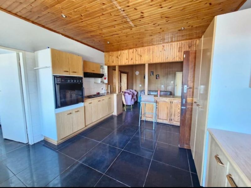 A functional kitchen featuring wooden cabinetry, built-in oven, hob, and extractor fan, finished with dark floor tiles and extensive wooden ceiling paneling.