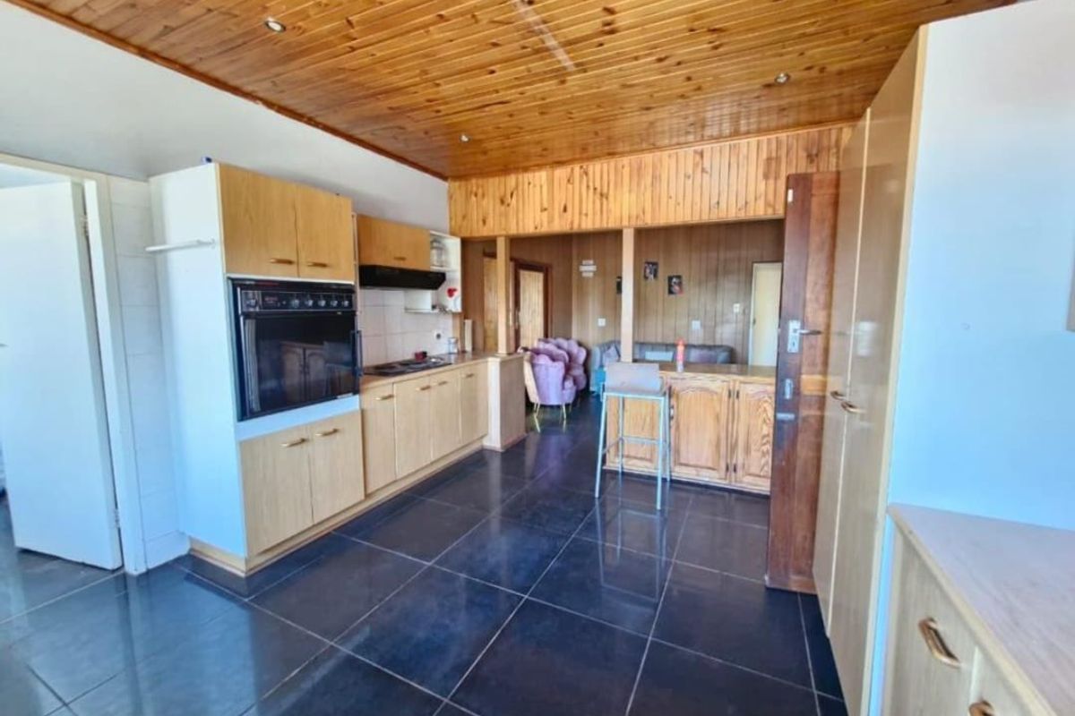 A functional kitchen featuring wooden cabinetry, built-in oven, hob, and extractor fan, finished with dark floor tiles and extensive wooden ceiling paneling.