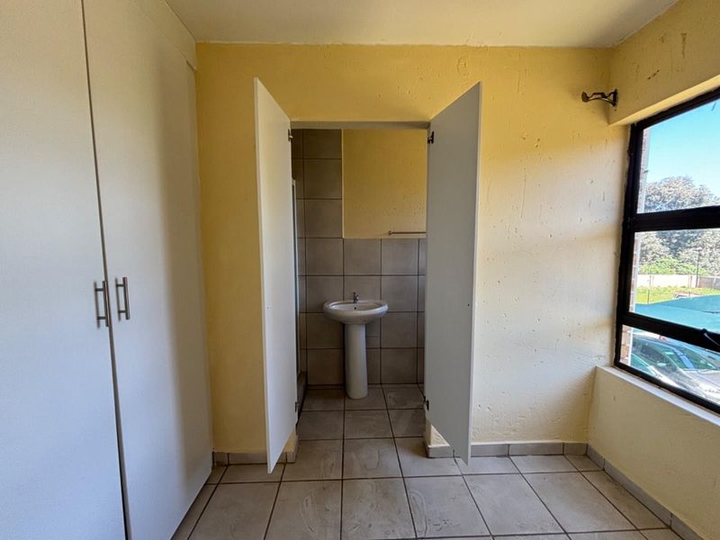 A bedroom featuring built-in cupboards and an en-suite bathroom with a pedestal basin and tiled flooring.