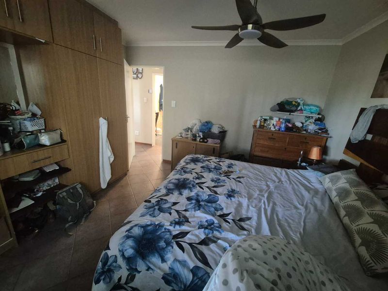 A bedroom featuring built-in cupboards, a ceiling fan, and tiled flooring, with direct access to an adjoining room.