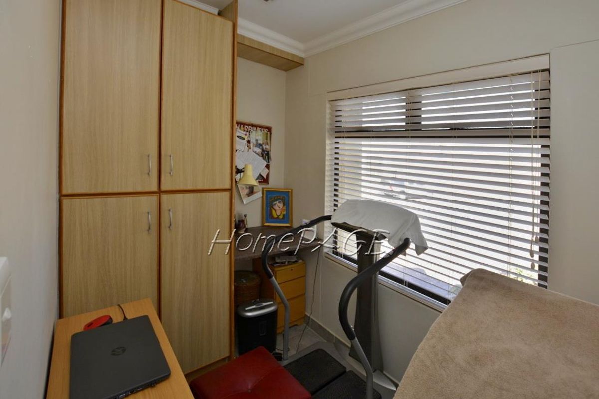 A compact bedroom or study featuring built-in wooden cabinetry and horizontal window blinds, providing functional storage and natural light.