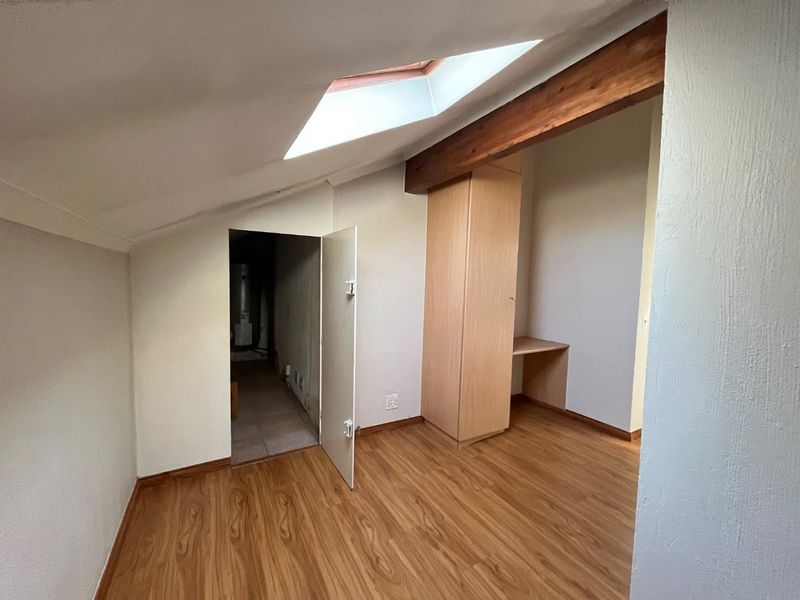 An attic-style bedroom featuring a sloped ceiling with a skylight, exposed timber beam, laminate flooring, and built-in cabinetry with a desk area.