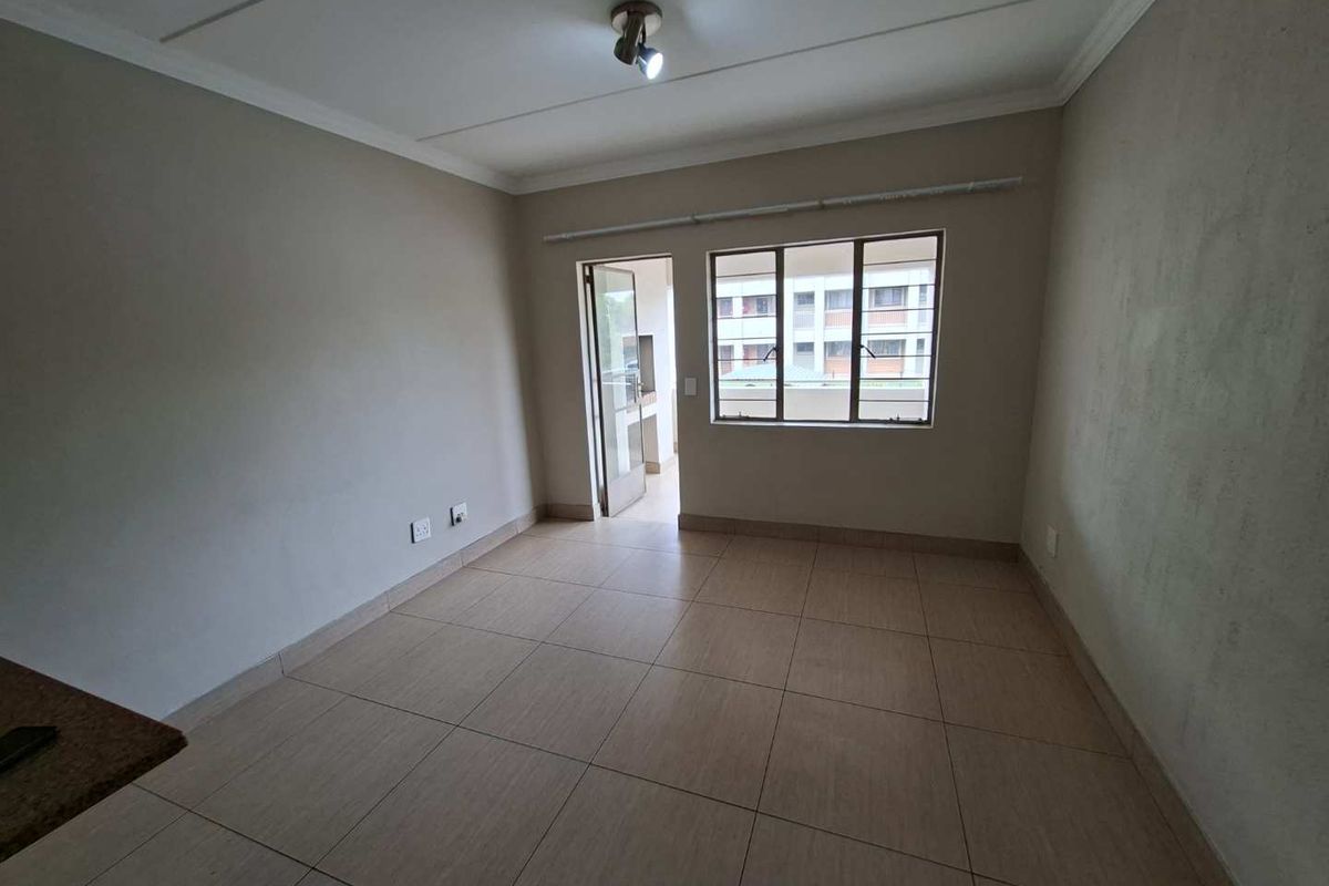 A bright, empty living area featuring neutral tiled flooring, a ceiling-mounted light fixture, and direct access to an outdoor balcony area.