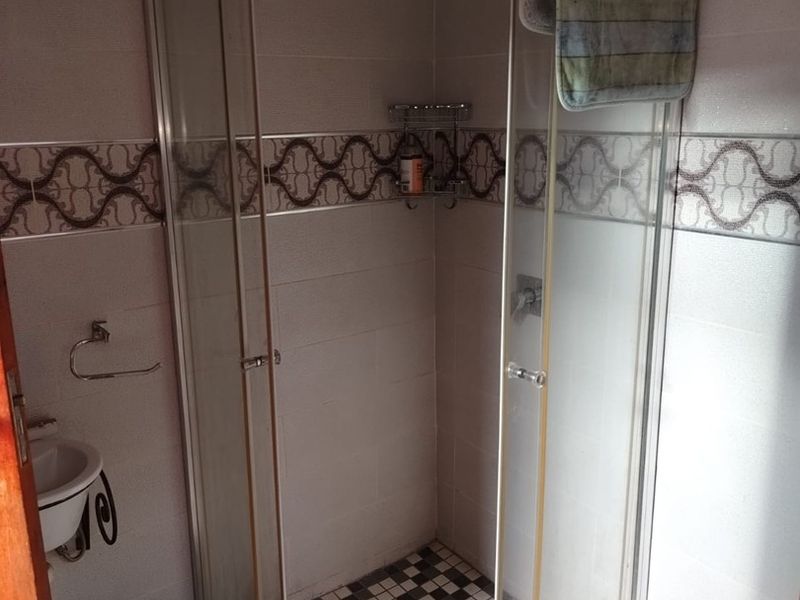 A functional bathroom featuring a glass-enclosed shower with a rain shower head, decorative wall tiling, and a checkered floor pattern.