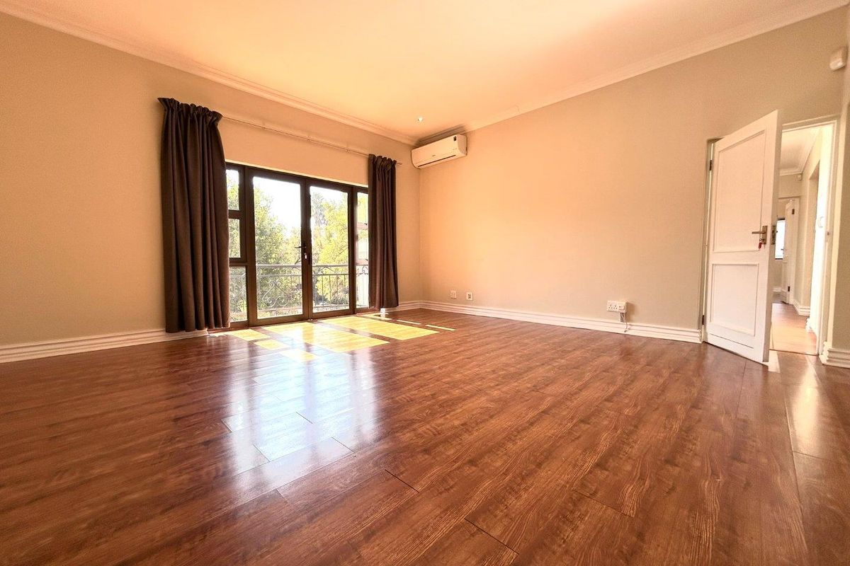 Spacious bedroom featuring warm laminate flooring, an air conditioning unit, and a sliding glass door leading to a private balcony.