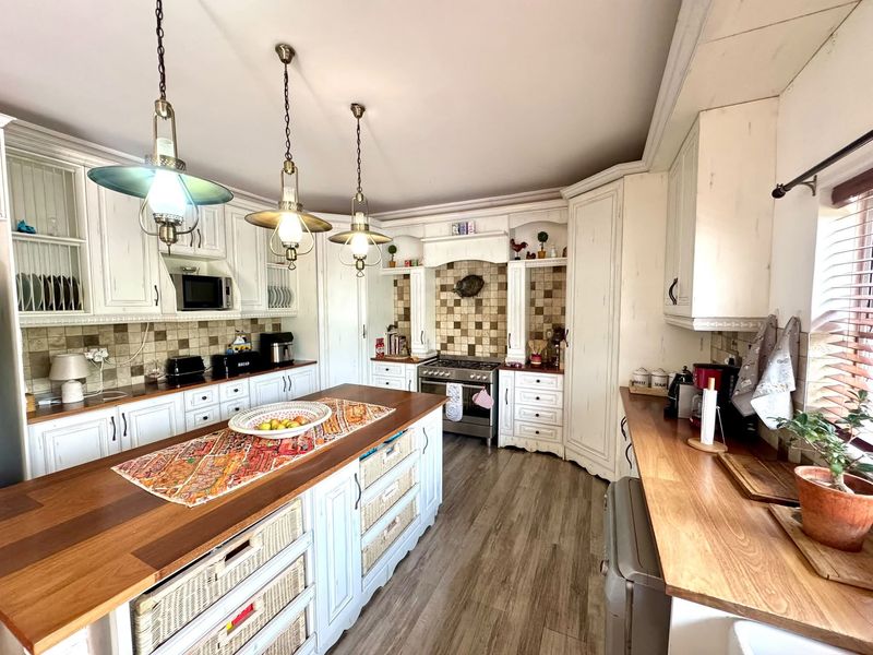 A well-appointed kitchen featuring white cabinetry, wooden countertops, a central island, tiled backsplash, and integrated appliances with warm pendant lighting.