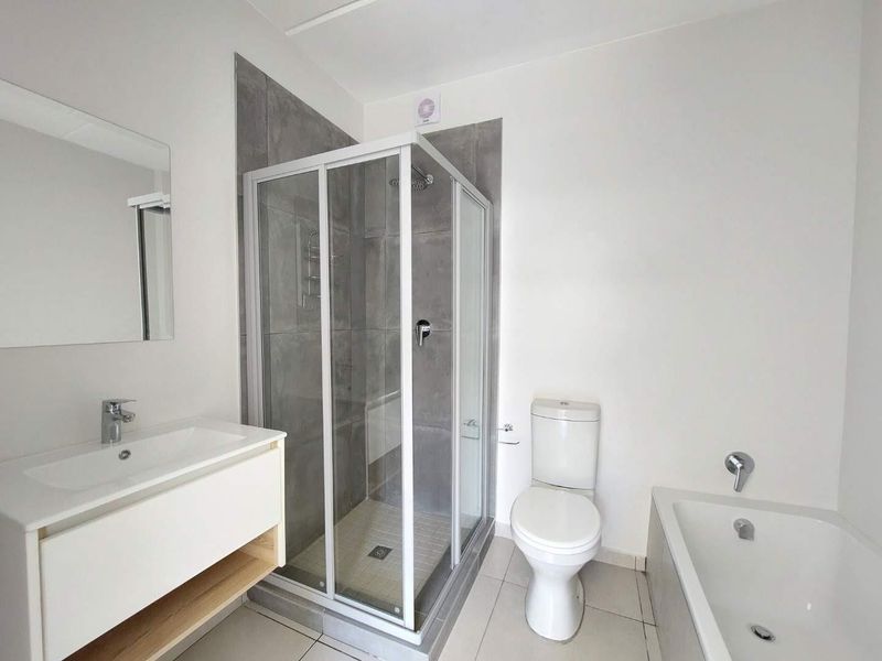 Modern bathroom featuring a glass shower enclosure, a sleek vanity basin, a toilet, and a bathtub with neutral grey tiling.