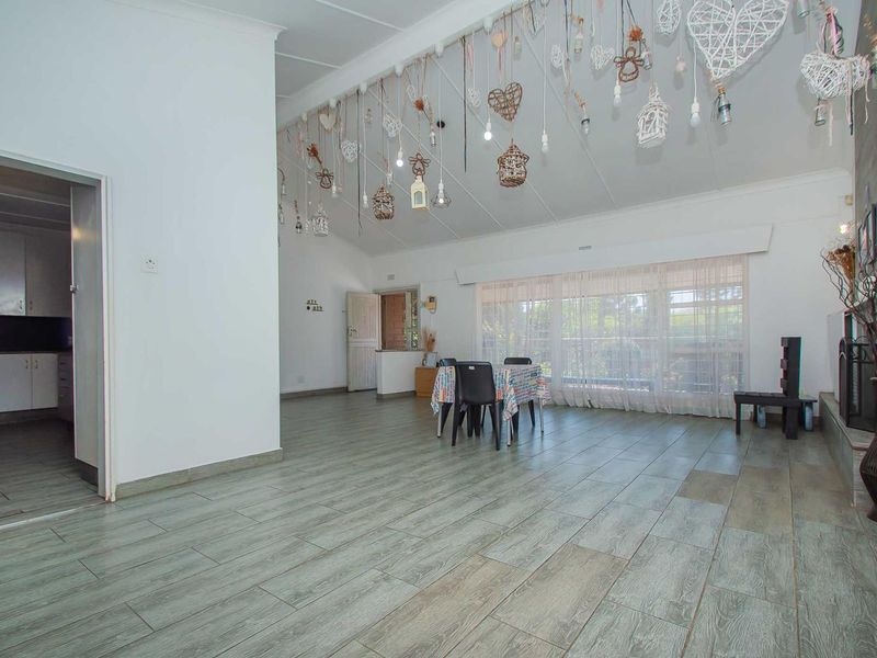 Spacious open-plan living and dining area featuring vaulted ceilings, tiled flooring, and a fireplace, with an adjacent kitchen visible.
