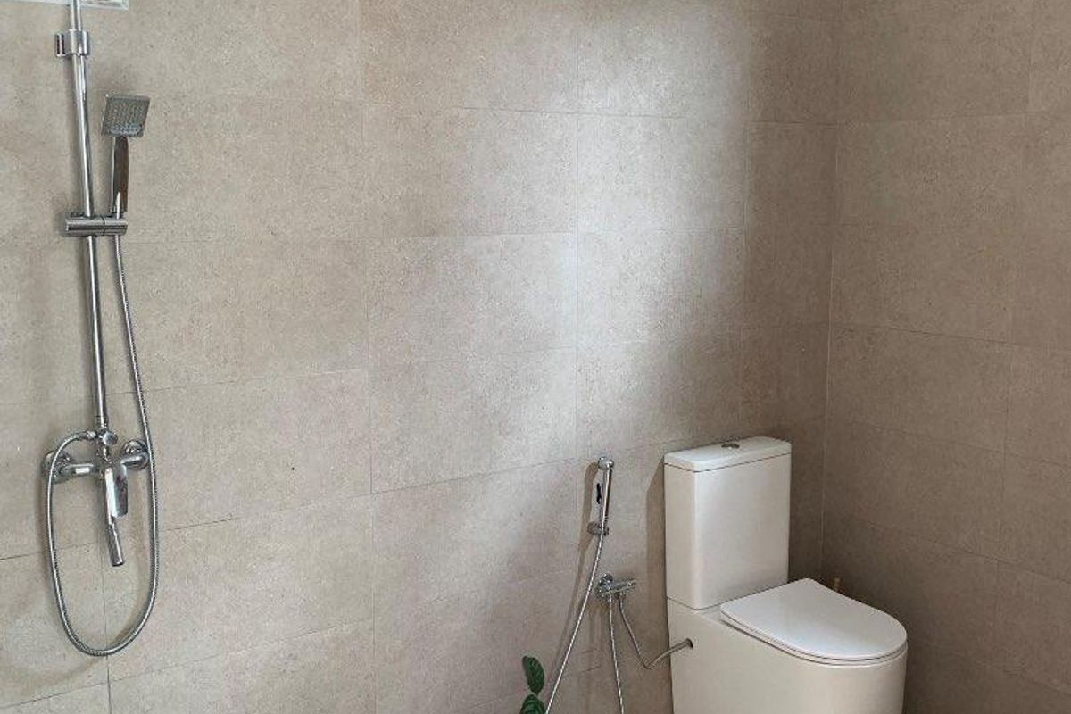 A modern bathroom featuring floor-to-ceiling neutral tiling, a wall-mounted rainfall shower system, and a sleek white toilet with a bidet spray.