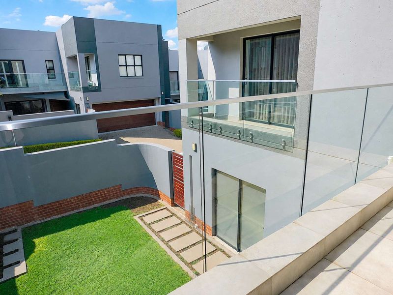 A modern rear exterior view featuring a glass balustrade, tiled patio area, and a small private garden with a paved walkway.
