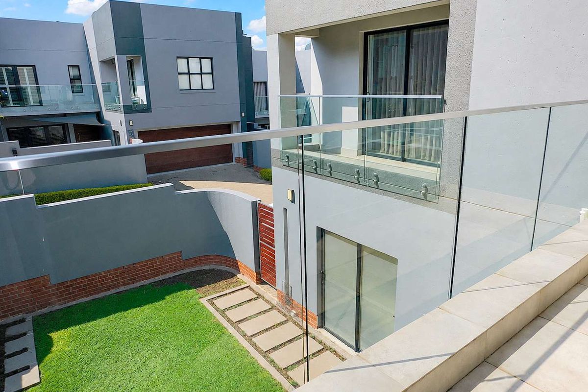 A modern rear exterior view featuring a glass balustrade, tiled patio area, and a small private garden with a paved walkway.