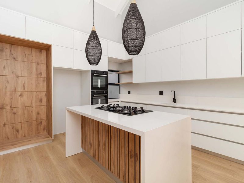 Modern kitchen featuring a central island with gas cooktop, sleek white cabinetry, built-in double ovens, and timber accents, offering a clean and contemporary aesthetic.