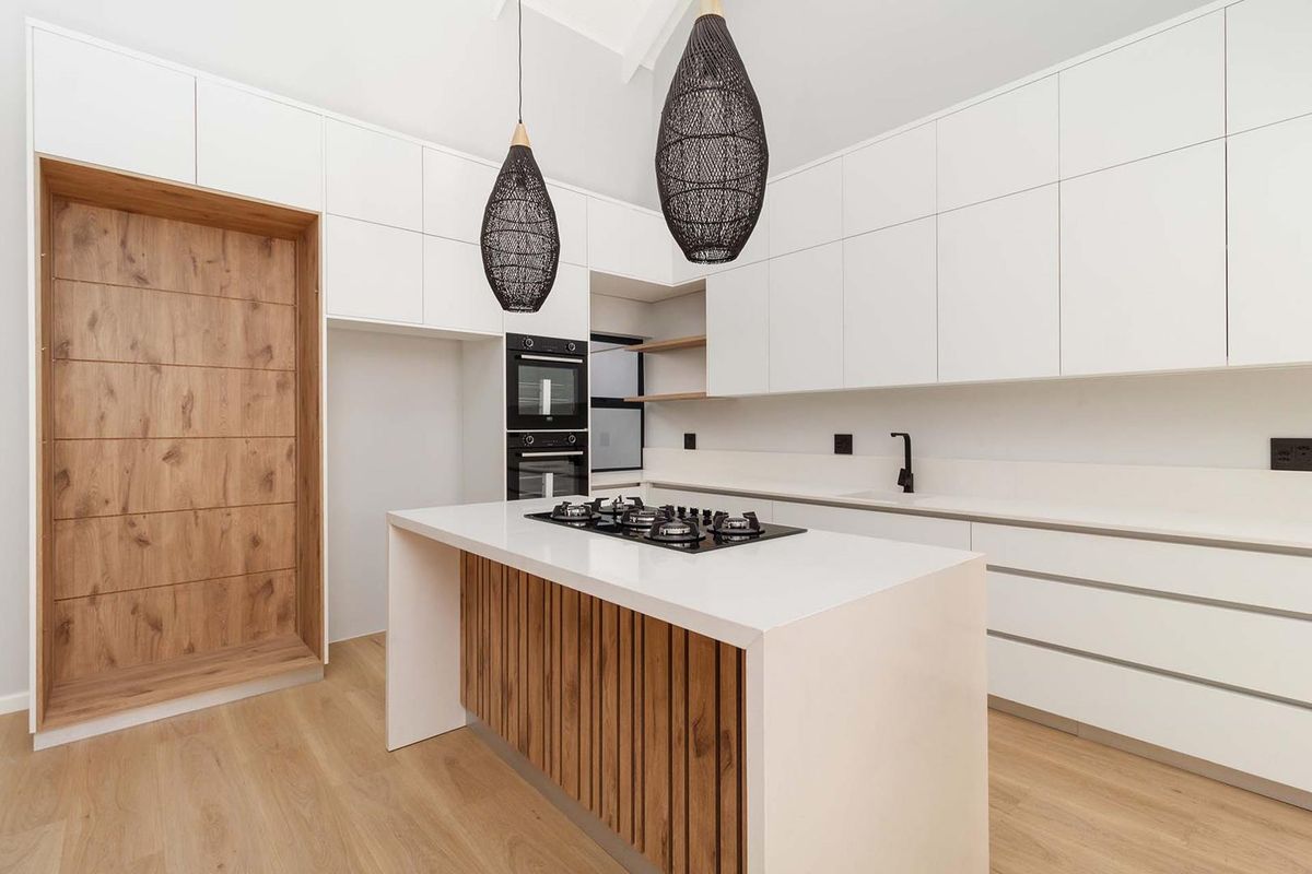 Modern kitchen featuring a central island with gas cooktop, sleek white cabinetry, built-in double ovens, and timber accents, offering a clean and contemporary aesthetic.