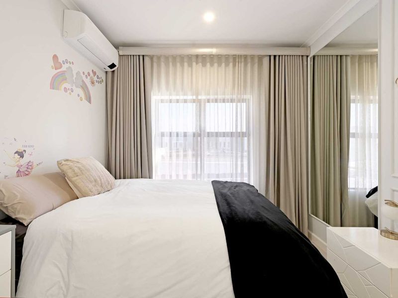 A well-maintained bedroom featuring a split-system air conditioner, floor-to-ceiling curtains, and a large mirrored built-in wardrobe.