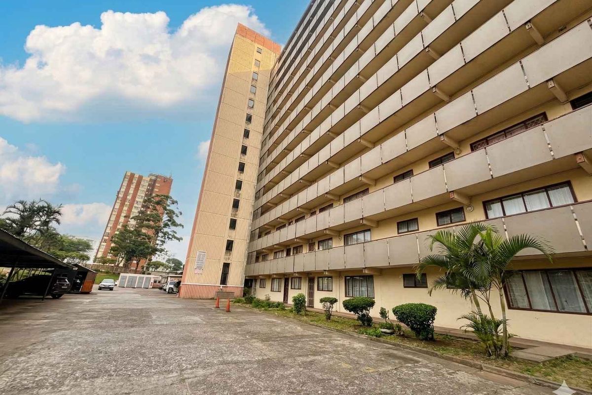 Exterior view of a multi-story apartment building featuring concrete balconies and an adjacent paved parking area.