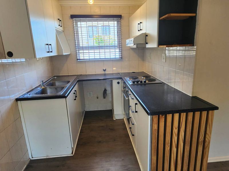 A compact, functional kitchen featuring built-in cabinetry, laminate countertops, a stainless steel sink, and an integrated electric hob and oven.