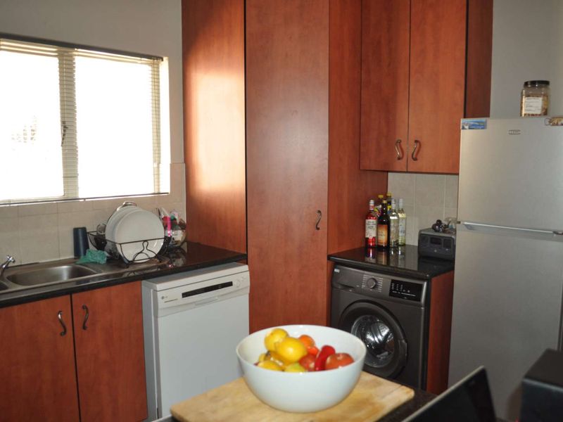 Functional kitchen featuring dark granite countertops, wood-finish cabinetry, tiled backsplash, and integrated space for laundry and dishwashing appliances.