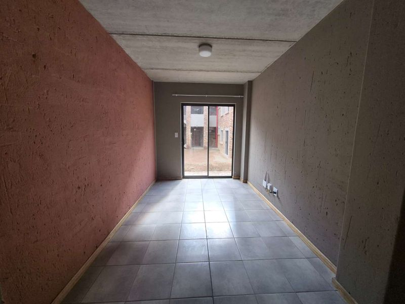 An empty living room featuring ceramic tiled flooring, exposed concrete ceiling, and a sliding glass door providing access to the exterior.