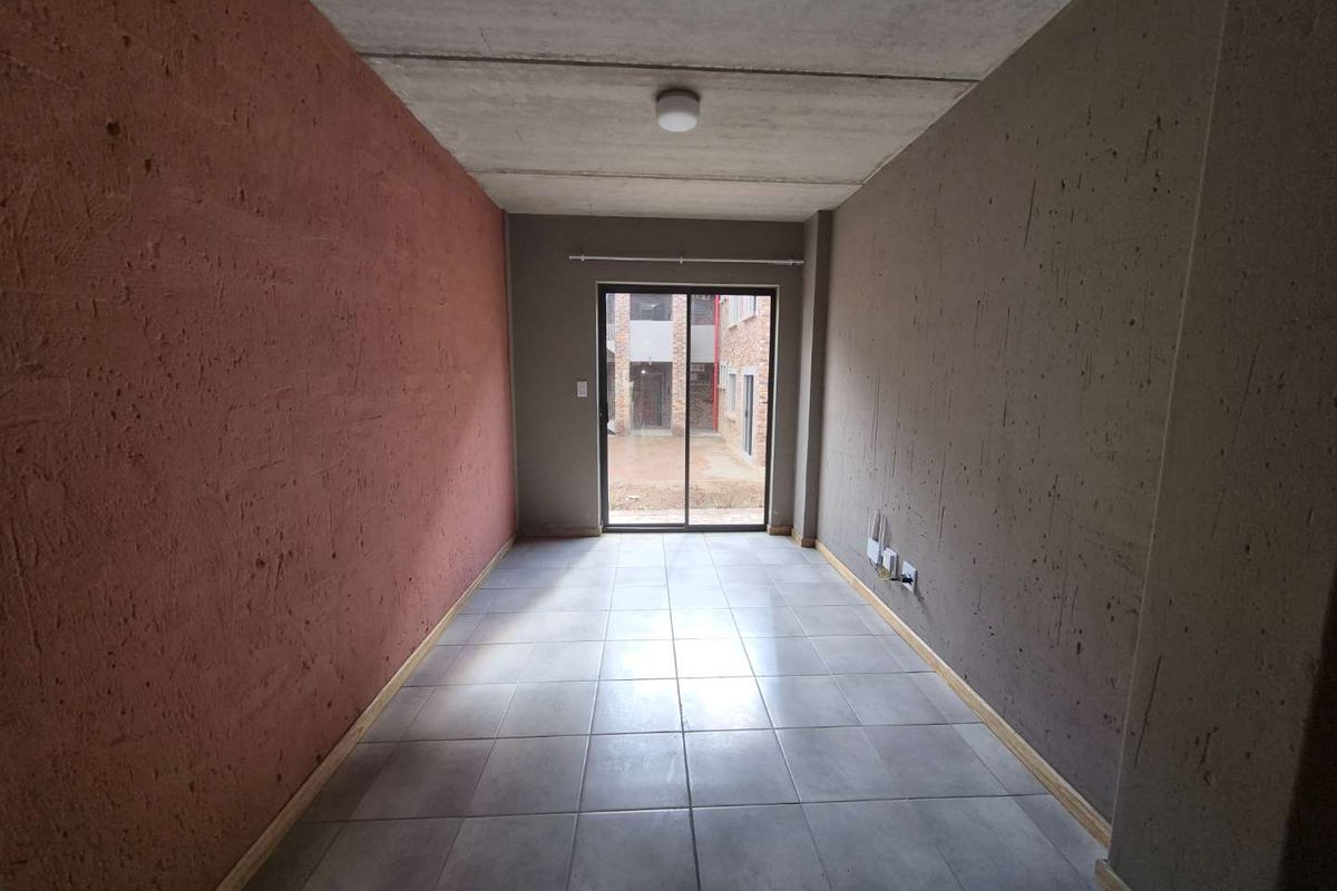 An empty living room featuring ceramic tiled flooring, exposed concrete ceiling, and a sliding glass door providing access to the exterior.
