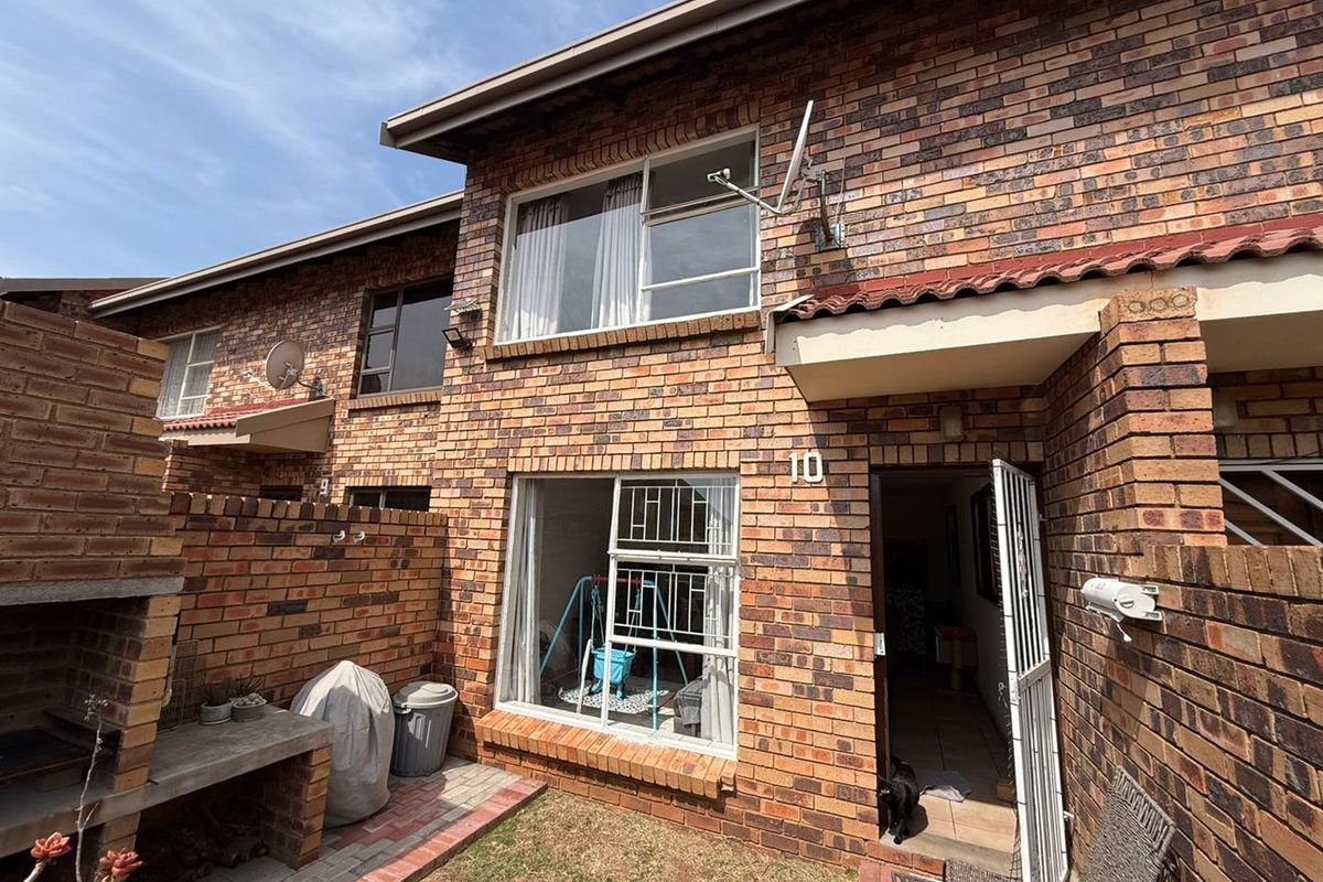 Rear view of a face brick cluster unit featuring a built-in brick braai, security gates, and a small private garden area.