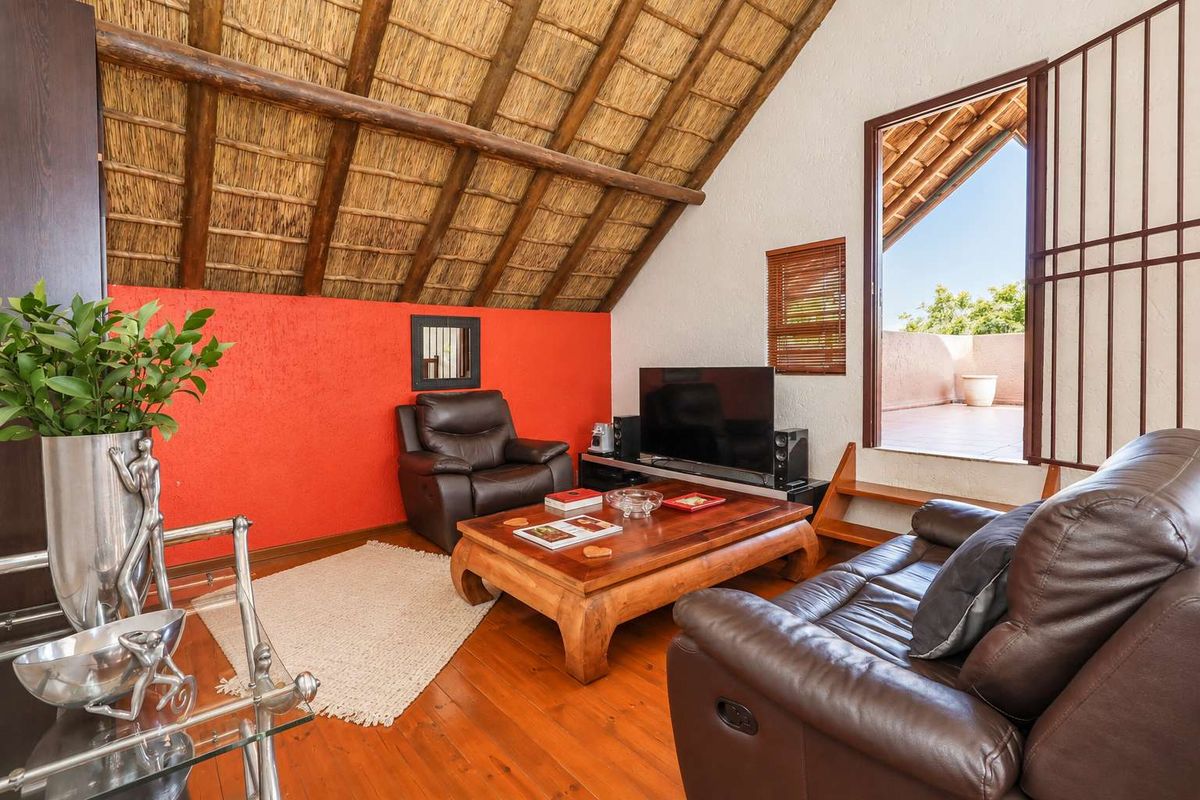 Living room featuring a high-pitched exposed thatch roof with timber rafters, hardwood flooring, and direct access to an outdoor balcony area.