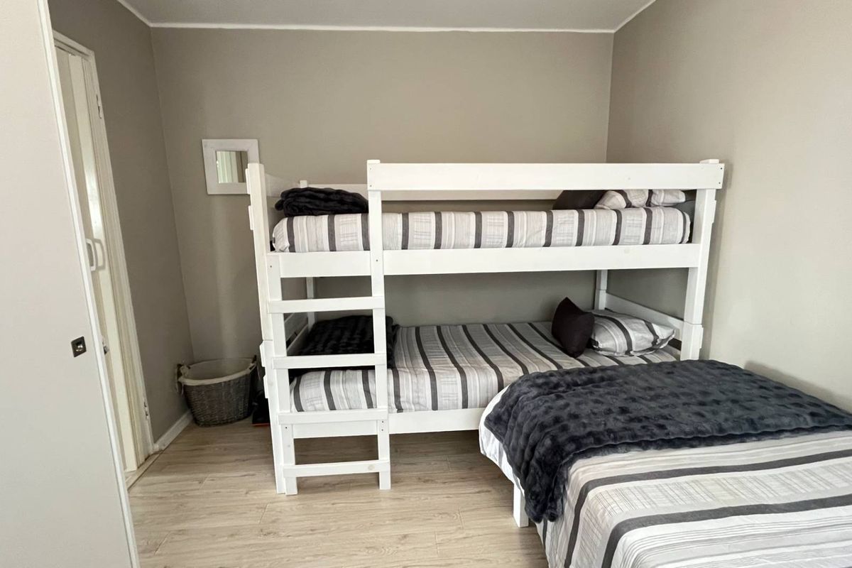 A functional bedroom featuring light-toned laminate flooring and neutral wall finishes, currently configured with multiple sleeping arrangements.