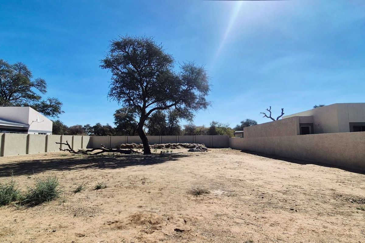A vacant residential plot featuring a perimeter boundary wall and a mature tree, offering a blank canvas for future development.