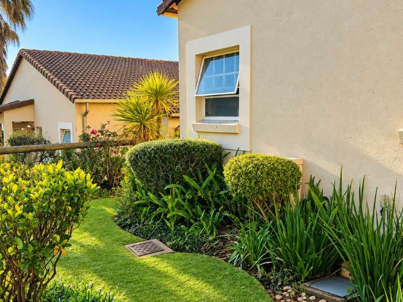 A well-maintained rear garden area featuring manicured lawn, established shrubs, and a clear view of the townhouse exterior wall and tiled roof.