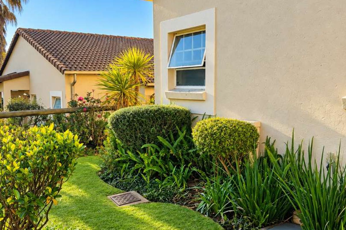 A well-maintained rear garden area featuring manicured lawn, established shrubs, and a clear view of the townhouse exterior wall and tiled roof.