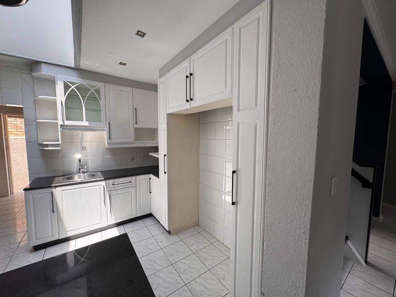 A clean, well-lit kitchen featuring white cabinetry, black granite countertops, tiled backsplash, and dedicated space for a refrigerator.