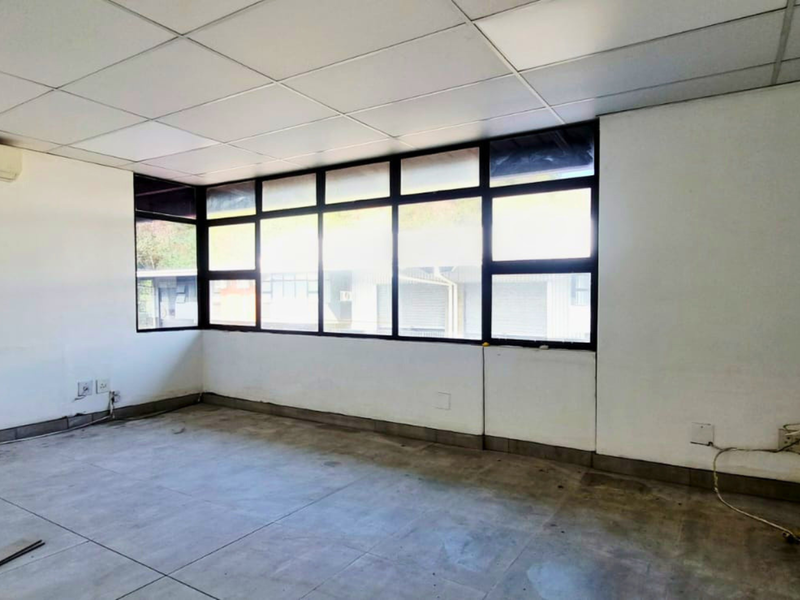 An empty industrial office space featuring a suspended ceiling, split-system air conditioning, and large windows providing ample natural light.