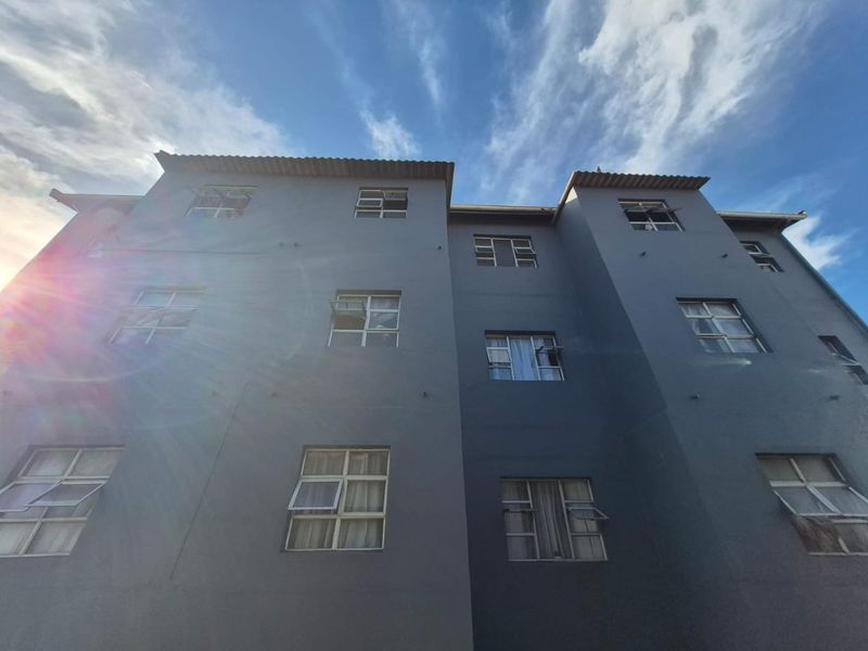 Low angle view of the apartment building exterior featuring grey painted facade and multiple casement windows under a clear blue sky.