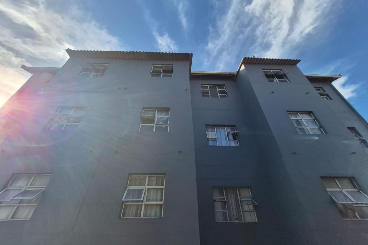 Low angle view of the apartment building exterior featuring grey painted facade and multiple casement windows under a clear blue sky.