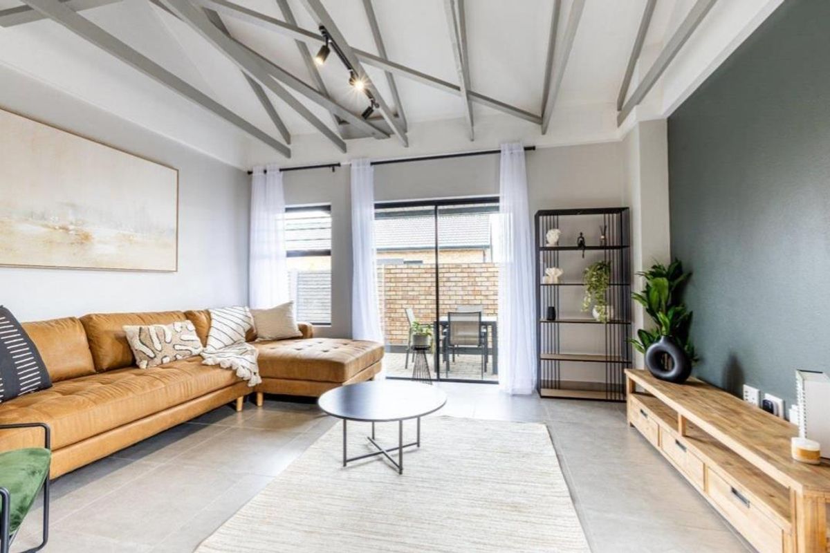 Modern living room featuring high ceilings with exposed beams, track lighting, large format floor tiles, and sliding doors leading to an outdoor patio area.