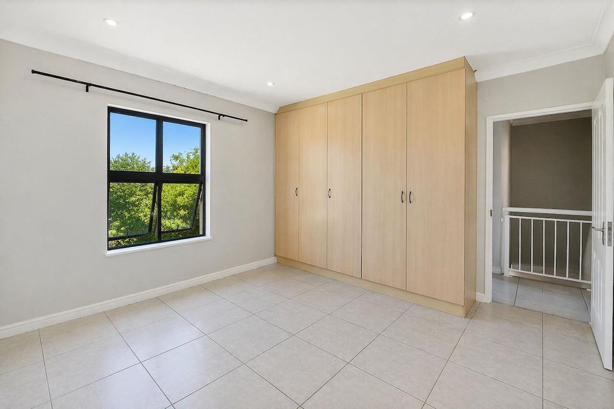 A bright, empty bedroom featuring neutral tiled flooring, recessed downlights, and a large built-in wardrobe with light wood-finish cabinetry.