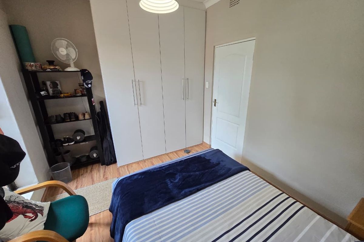 A functional bedroom featuring built-in wardrobes, laminate flooring, and a standard interior door.