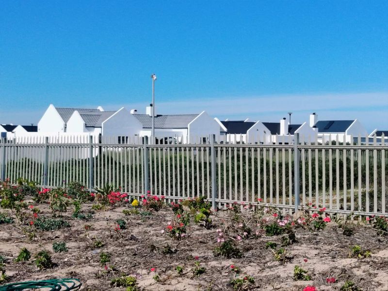 A view of the rear exterior of a residential property featuring white facades, pitched roofs, and secure metal perimeter fencing.
