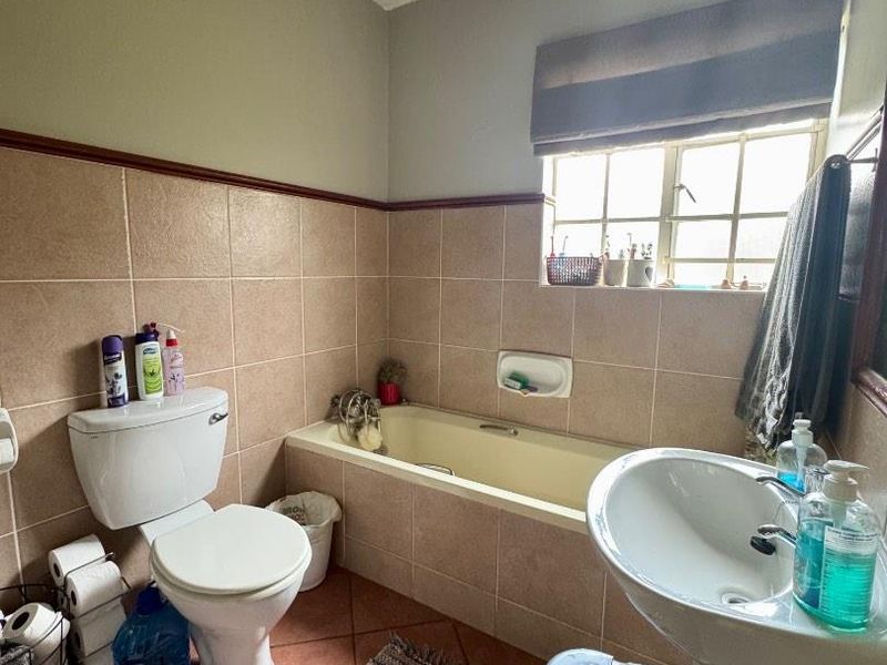 A functional bathroom featuring a bathtub, pedestal basin, and toilet with tiled finishes, offering a dated but practical layout.