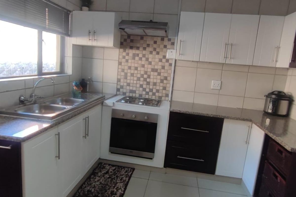 A functional kitchen featuring white and dark cabinetry, granite countertops, a built-in oven with gas hob, and a tiled backsplash.