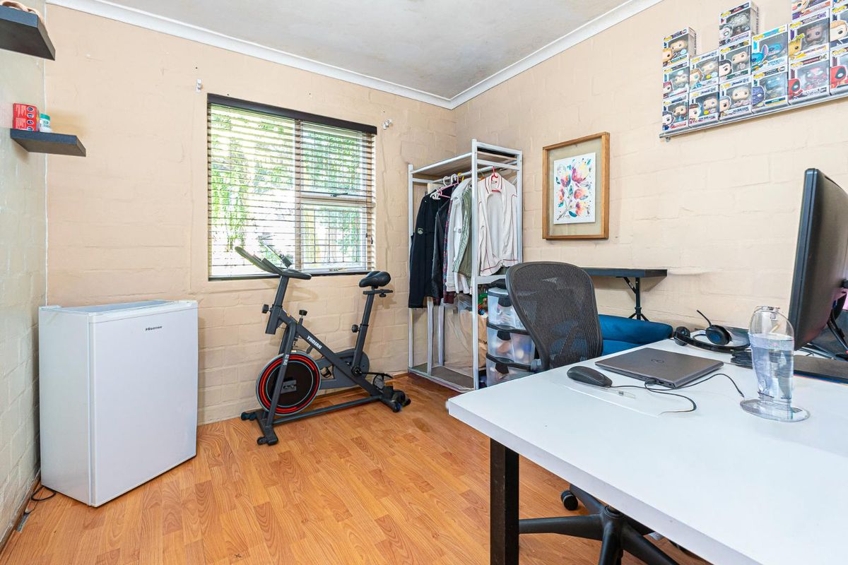 A bedroom featuring laminate flooring and painted brick walls, currently utilized as a multi-purpose home office and exercise space.