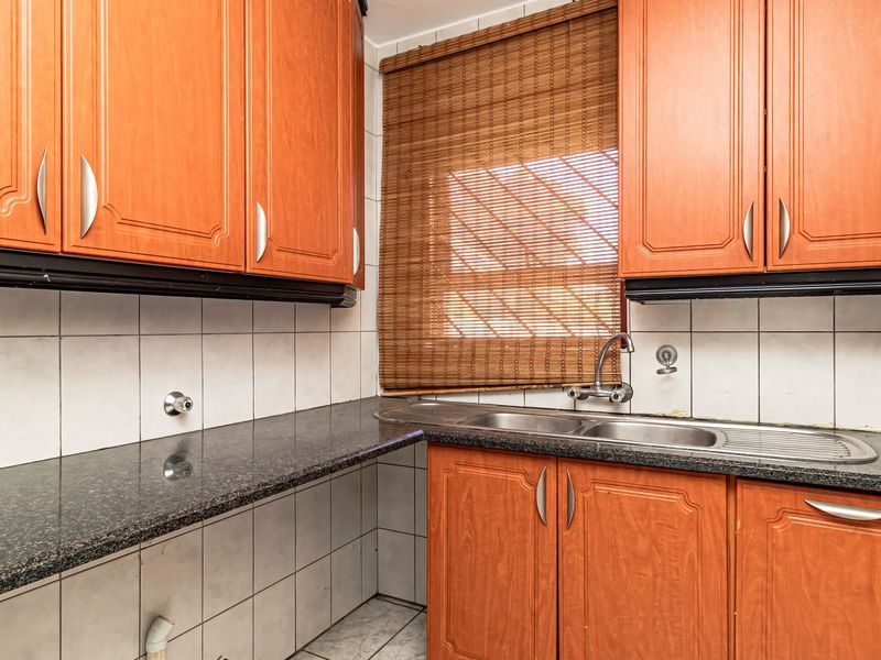 A functional scullery area featuring laminate cabinetry, granite countertops, and a stainless steel double sink with tiled backsplash and flooring.