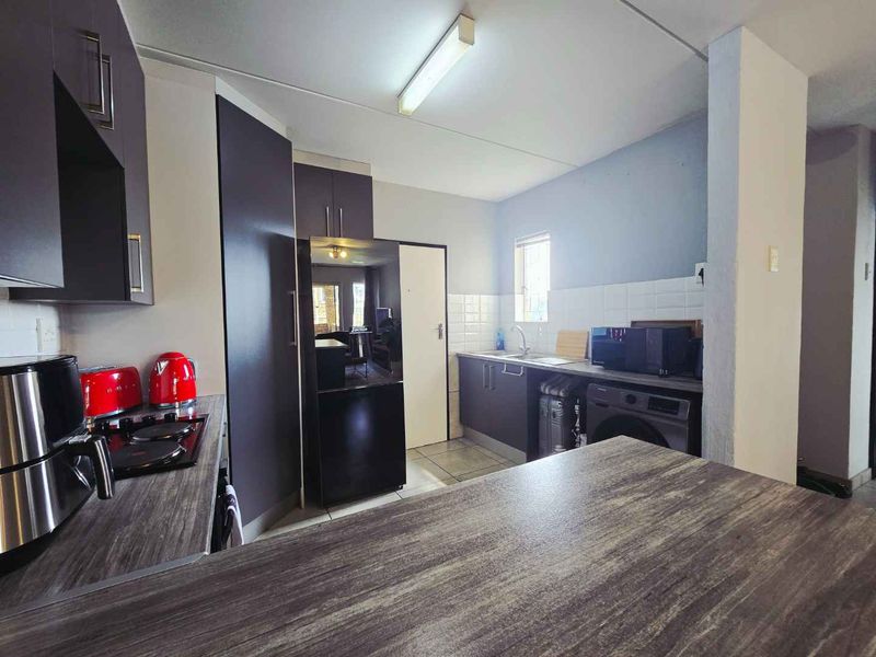 A functional kitchen featuring dark cabinetry, laminate countertops, a tiled backsplash, and integrated plumbing for appliances.