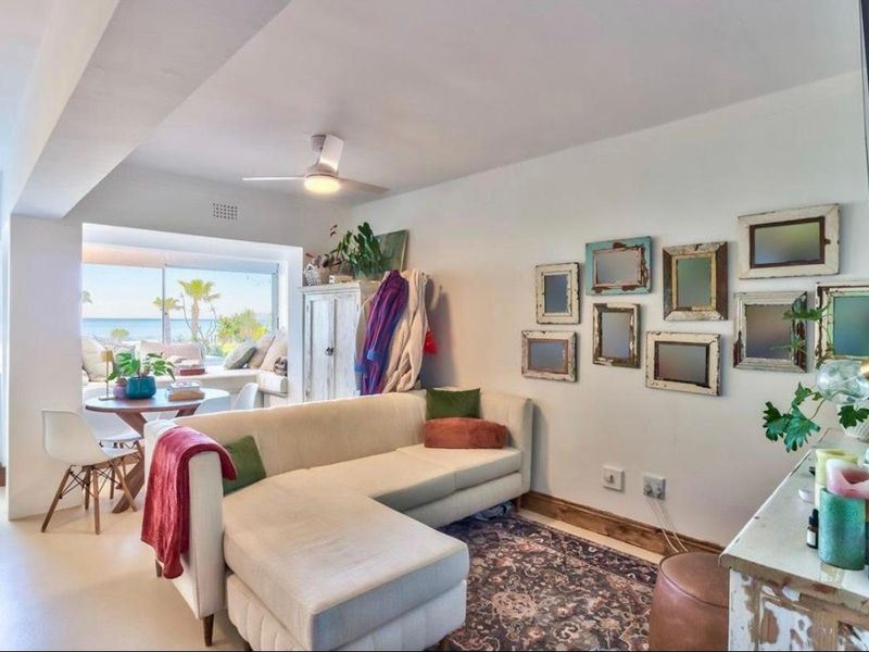 Bright open-plan living area featuring a ceiling fan, neutral flooring, and large sliding glass doors that provide natural light and ocean views.
