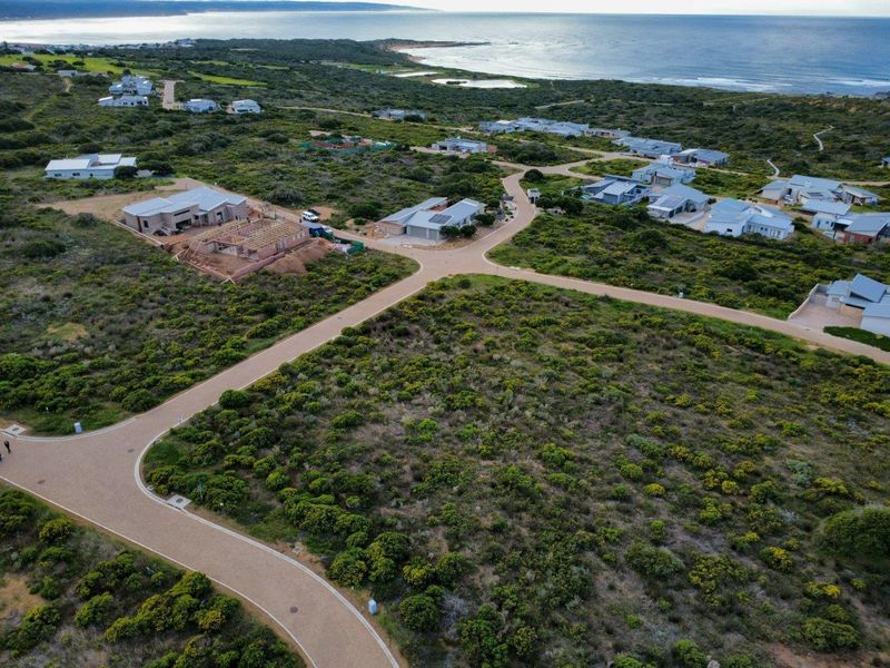 Aerial view of a residential estate featuring paved roads and coastal landscape, showcasing the surrounding neighborhood and proximity to the ocean.