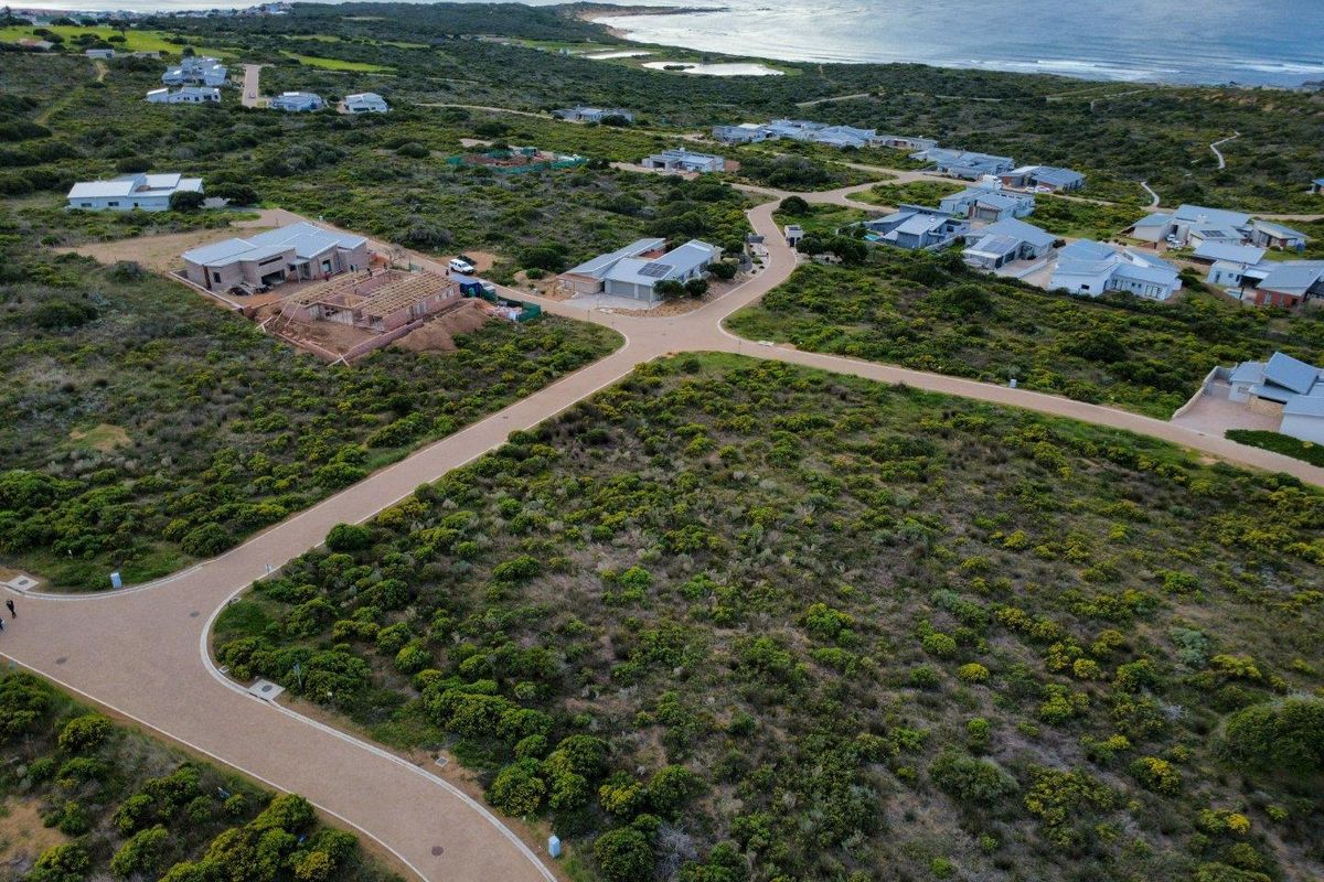 Aerial view of a residential estate featuring paved roads and coastal landscape, showcasing the surrounding neighborhood and proximity to the ocean.