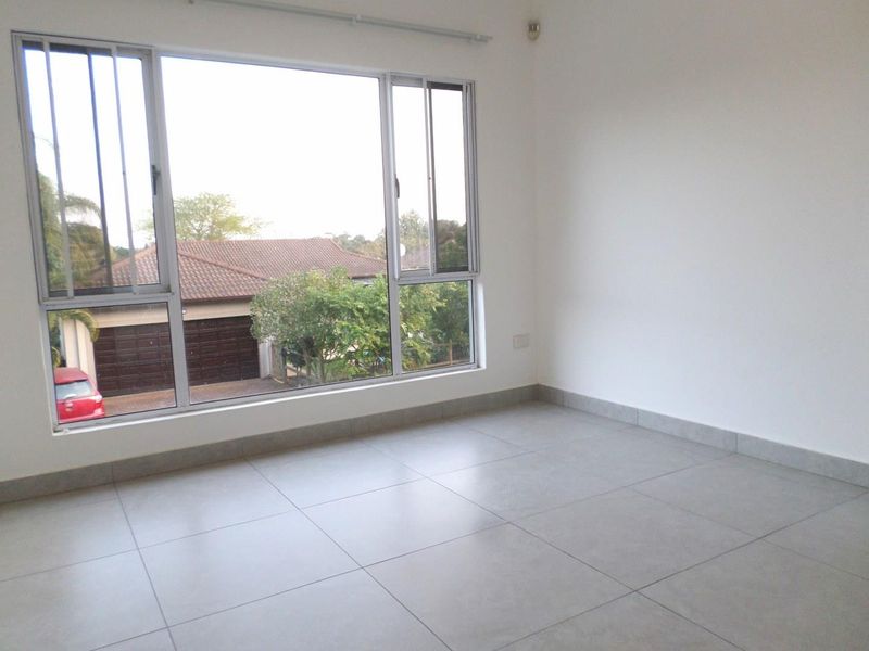 A bright, empty bedroom featuring large aluminium-framed windows and neutral tiled flooring, offering a clean and modern blank canvas.