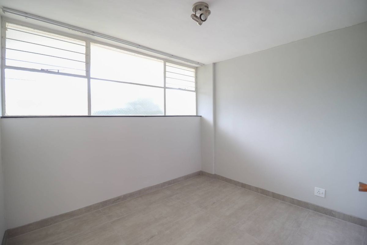 A bright, empty bedroom featuring neutral tiled flooring, clean walls, and a large window providing ample natural light.