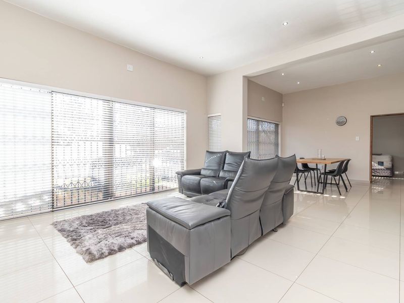 Spacious open-plan living and dining area featuring large sliding glass doors, neutral tiled flooring, and modern recessed downlighting throughout.